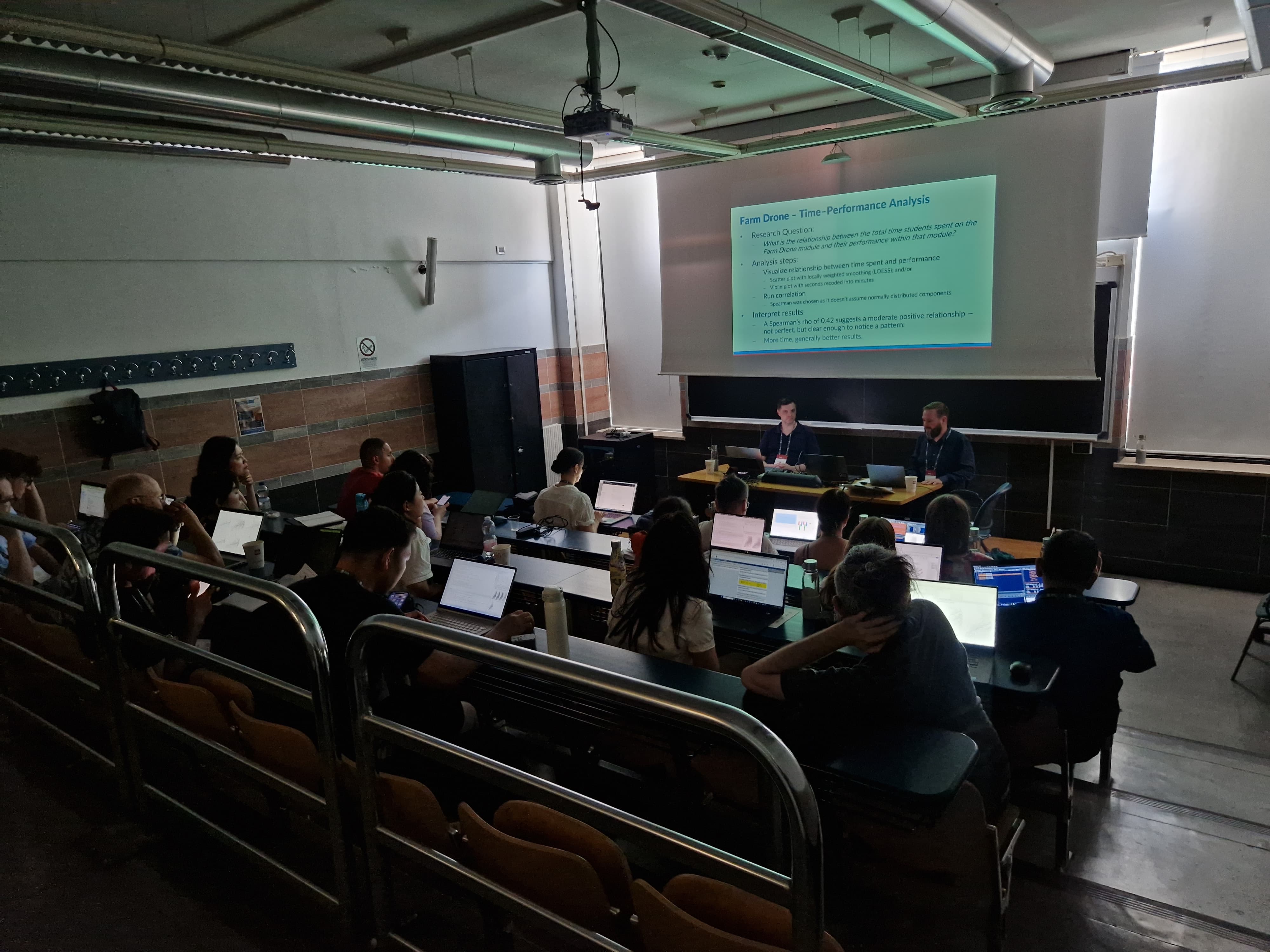  alt="Image of workshop speakers and audience in a dimly lighted room">