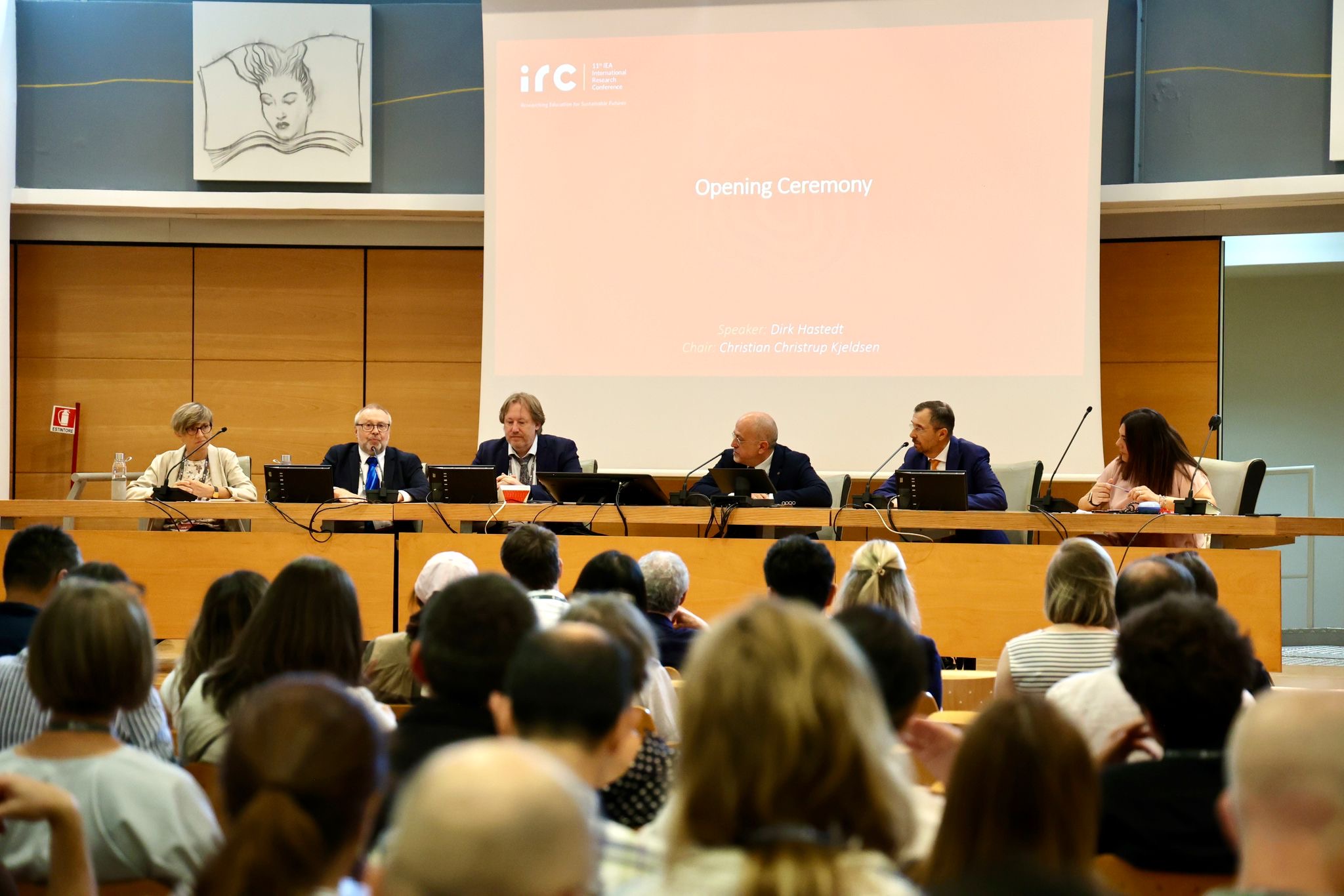 Six speakers sitting at a half circle desk with gooseneck microphones